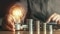 A hand holds a light bulb next to stacks of coins