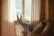 The picture shows a man with a book in his hands, sitting on an armchair in front of a window with his legs on a radiator.